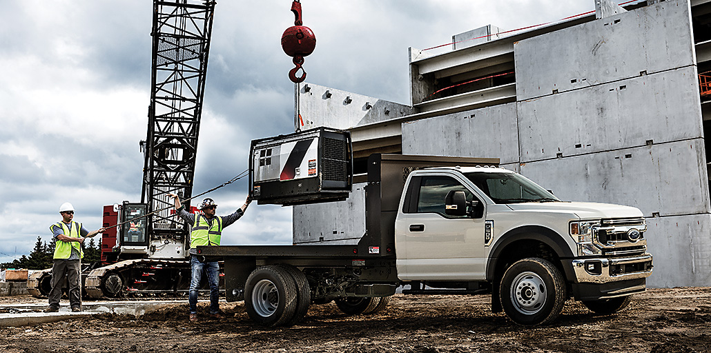 Workers use a crane to lower heavy equipment onto a Super Duty chassis flatbed truck.