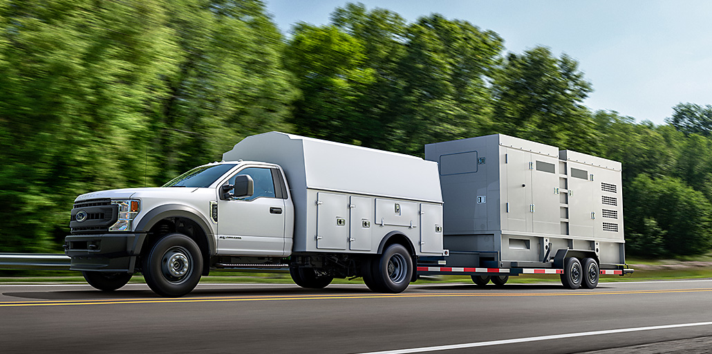 Ford Super Duty Chassis with a service body is driving down the highway with a trailer.