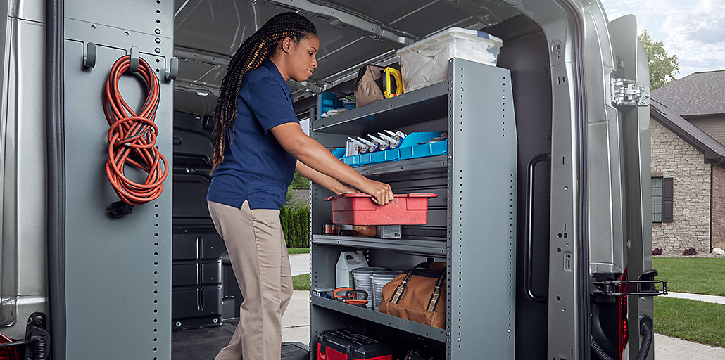 A construction worker with a hard hat retrieves equipment from the racks and bins in his 2020 Ford Transit.